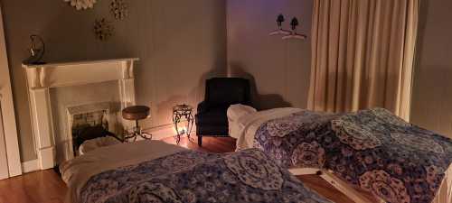 A cozy spa room with two massage tables, soft lighting, and a fireplace, creating a relaxing atmosphere.