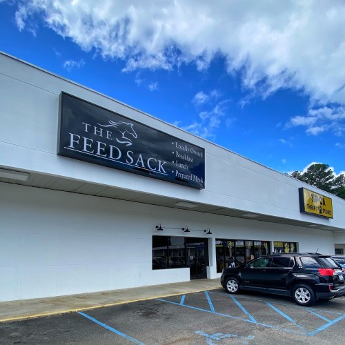 Exterior of a building featuring a sign for "The Feed Sack," promoting locally owned breakfast and prepared meals.