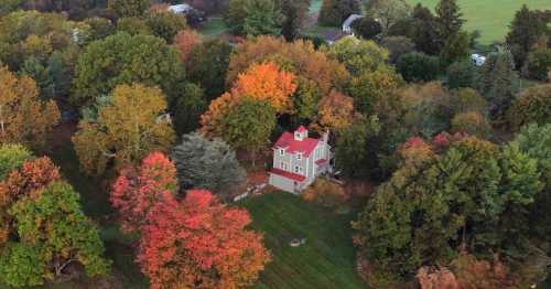 Aerial view of a house surrounded by vibrant autumn trees in shades of red, orange, and green.