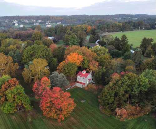 Aerial view of a house surrounded by vibrant autumn trees in a rural landscape.