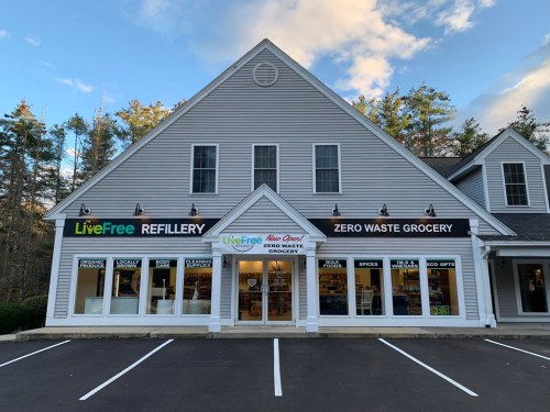 Exterior of a zero waste grocery store with large windows, featuring signs for "Live Free" and "Refillery."
