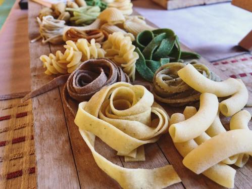 A variety of colorful pasta shapes arranged on a wooden board, showcasing different textures and colors.