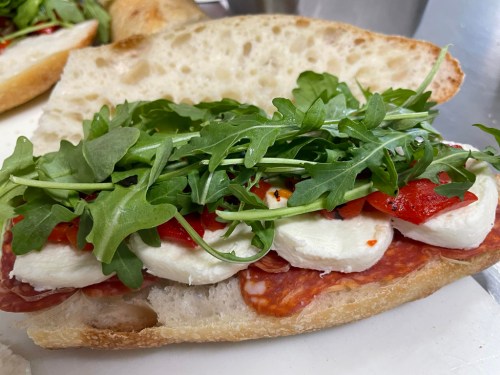 A sandwich with layers of salami, mozzarella, roasted red peppers, and fresh arugula on crusty bread.