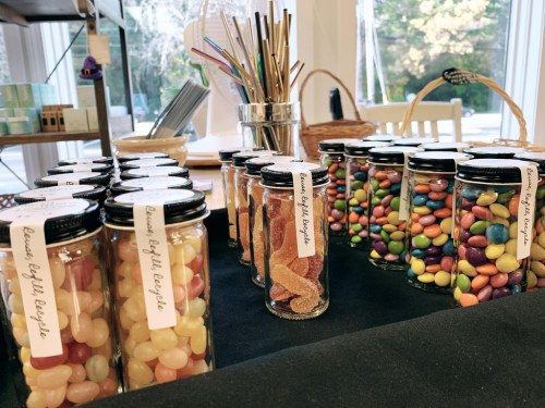 A display of colorful candy jars on a table, featuring jelly beans and assorted gummies with labels.