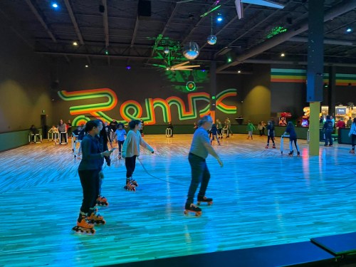 A roller skating rink with colorful lights, people skating, and a large "Remix" sign on the wall.