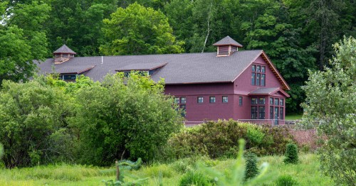 A large red building with multiple windows, surrounded by greenery and trees in a natural setting.