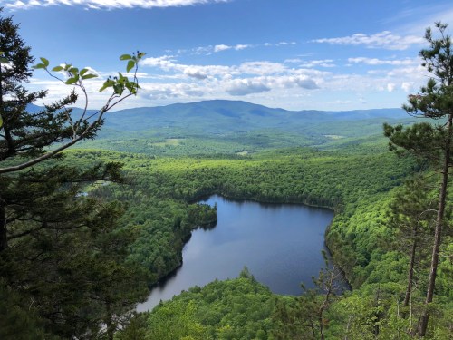 A scenic view of a lush green landscape with a tranquil lake surrounded by mountains under a blue sky.