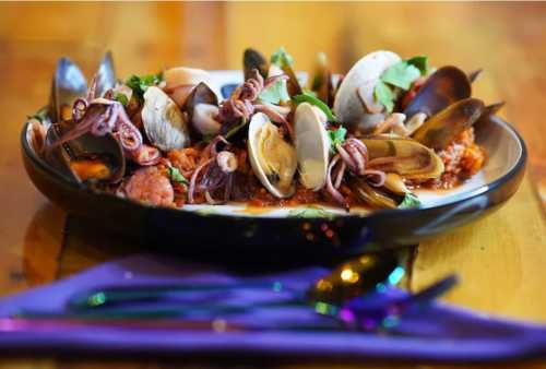 A vibrant seafood platter featuring clams, mussels, and octopus on a wooden table, garnished with herbs.