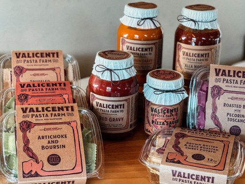 A variety of Valicenti Pasta Farm products, including sauces, pasta, and spreads, displayed on a wooden surface.