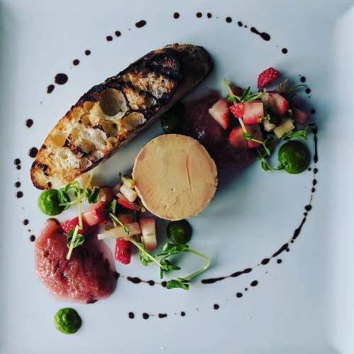 A gourmet dish featuring grilled bread, foie gras, fruit compote, and vibrant green sauce, elegantly arranged on a plate.
