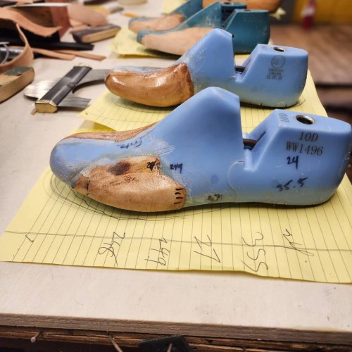 A row of blue shoe lasts on yellow paper, with handwritten notes and measurements visible beside them.
