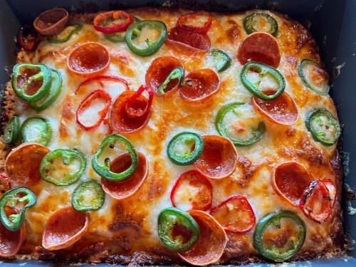 A baked dish topped with melted cheese, pepperoni, and colorful sliced peppers, including jalapeños and red bell peppers.