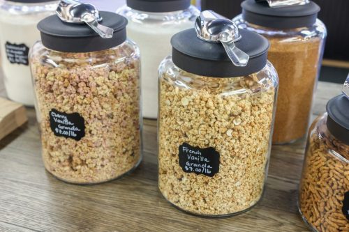 Two glass jars filled with colorful granola, labeled "Cherry Vanilla" and "French Vanilla," on a wooden surface.