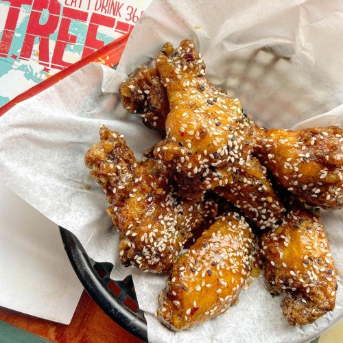 A basket of sesame-coated chicken wings on parchment paper, with a colorful menu in the background.