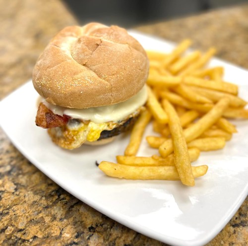 A burger with bacon and melted cheese on a bun, served with a side of golden French fries on a white plate.