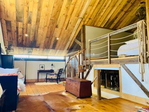 Cozy attic room with wooden beams, a bed, a small table, and a rustic chest, featuring warm, inviting decor.