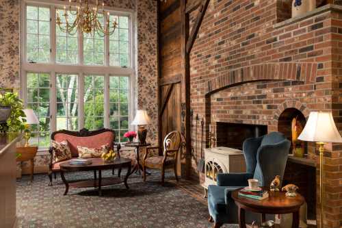 Cozy living room with a brick fireplace, floral wallpaper, elegant furniture, and large windows letting in natural light.