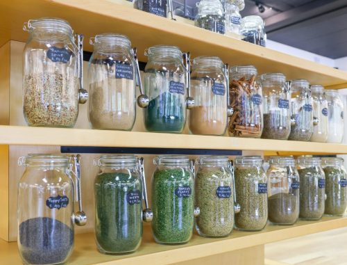 A wooden shelf displaying various jars filled with colorful spices and herbs, each labeled for easy identification.