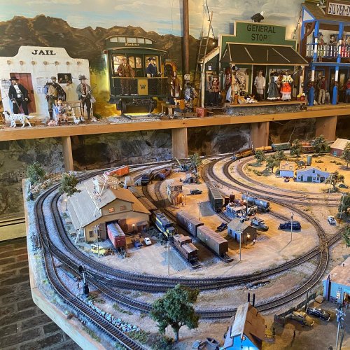 A detailed model train setup featuring buildings, tracks, and miniature figures in a Western-themed scene.