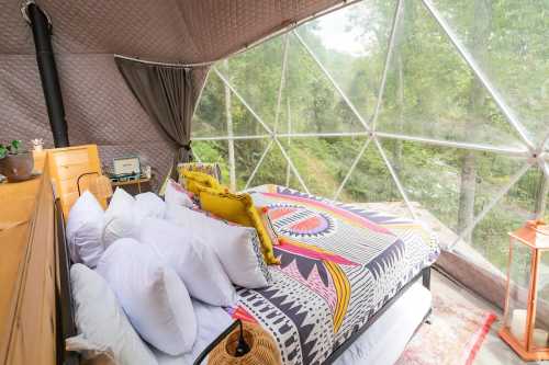 Cozy bedroom inside a geodesic dome, featuring a colorful bedspread and large windows overlooking a forested area.