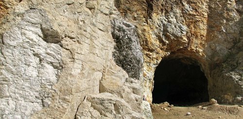 A rocky cave entrance surrounded by textured stone walls and earthy ground.