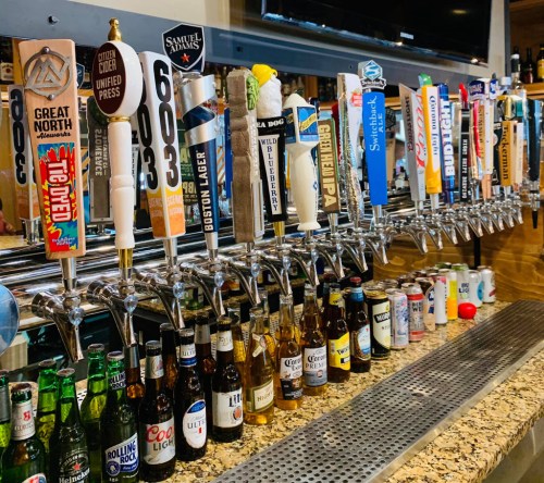 A bar with a variety of beer taps and bottles lined up on the counter, showcasing different brands and styles.