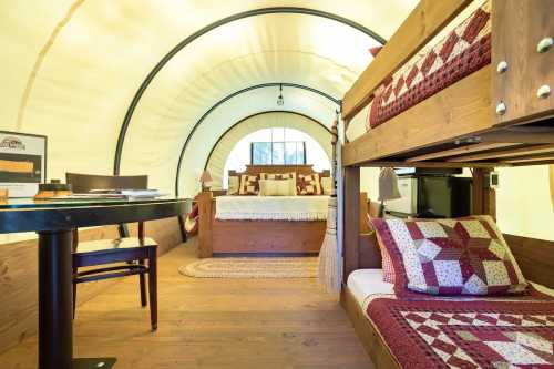 Cozy interior of a glamping tent featuring a bunk bed, a double bed, and a dining area with rustic decor.