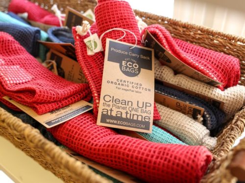 A basket filled with colorful organic cotton produce bags, each tagged with eco-friendly branding and messages.