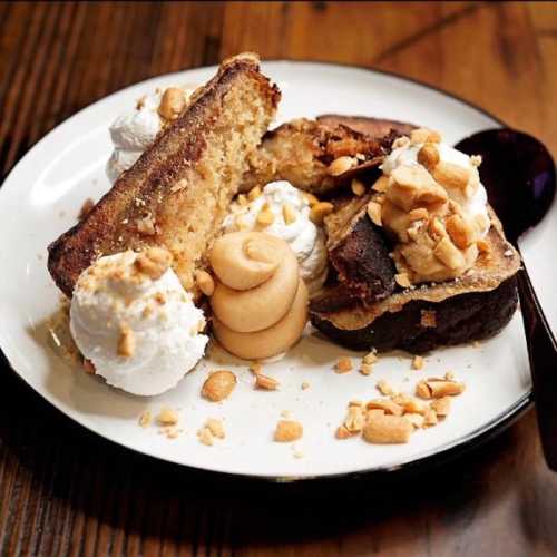 A plate of dessert featuring cake, whipped cream, and crushed peanuts, served with a spoon on a wooden table.