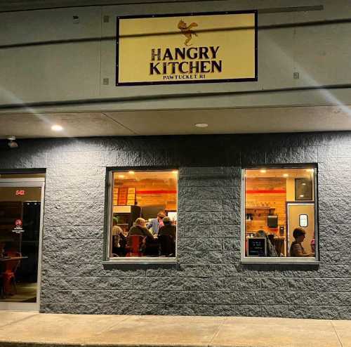 Exterior view of Hangry Kitchen in Pawtucket, RI, with a sign and people visible through the window.