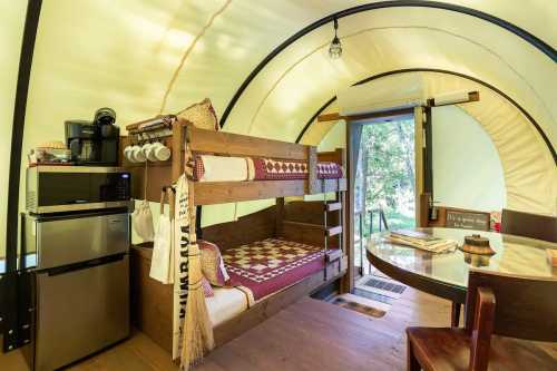 Cozy interior of a glamping tent featuring bunk beds, a kitchenette, and a dining table with natural light.