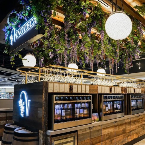 A stylish wine bar with hanging greenery, illuminated signs, and glassware displayed on wooden shelves.