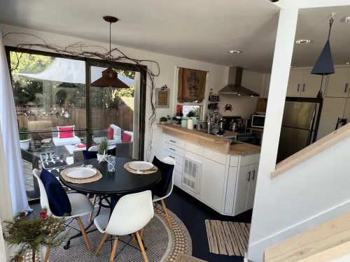 A modern kitchen and dining area with a round table, white chairs, and a view of an outdoor seating space.