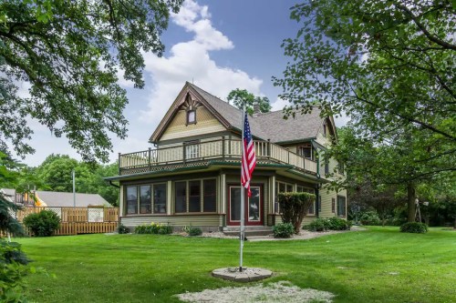 A charming two-story house with a porch, surrounded by greenery and featuring an American flag in the front yard.