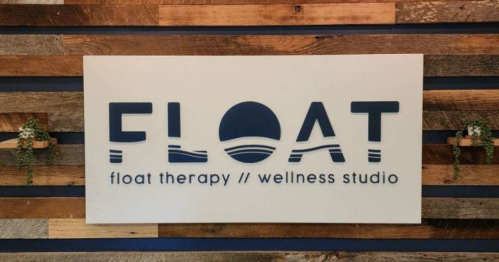Sign for "FLOAT" wellness studio featuring a modern design with wooden background and greenery accents.