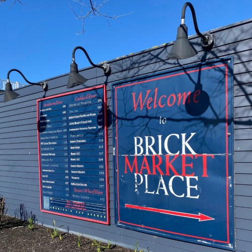 Signboard for Brick Marketplace displaying a list of shops and services, with a blue sky in the background.