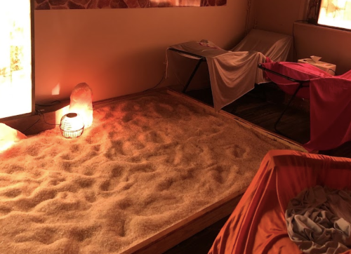 A cozy room with a sand area, soft lighting, and comfortable seating for relaxation or therapy.