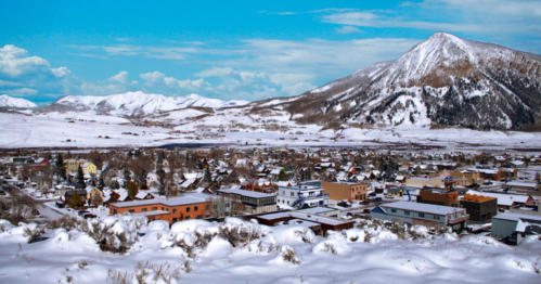 A snowy mountain landscape overlooking a small town with colorful buildings and a clear blue sky.