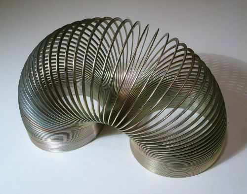 A metallic slinky toy arranged in a curved, wave-like shape, casting shadows on a white surface.