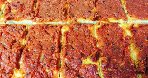 A close-up of a freshly baked pizza with a thick layer of red sauce and cheese, cut into rectangular slices.