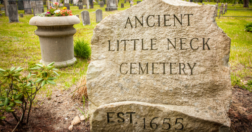 A stone monument reading "Ancient Little Neck Cemetery" with "EST. 1655" in a grassy cemetery setting.