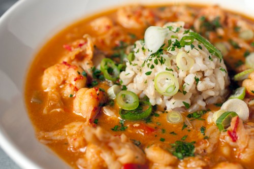 A bowl of shrimp gumbo with rice, garnished with green onions and herbs, in a rich, flavorful broth.