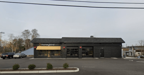A modern black building with a yellow awning labeled "honeybird" and a parking lot in front.