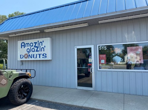 Exterior of Amazin' Glazin' Donuts shop with a blue roof and a military vehicle parked outside.