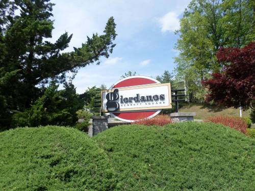 Sign for Giordano's in Kennett Square, surrounded by greenery and trees under a clear blue sky.