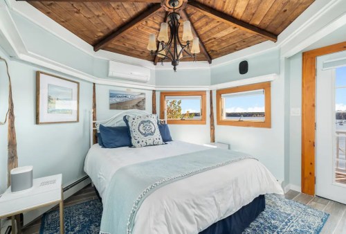 Cozy bedroom with a wooden ceiling, light blue walls, and large windows showcasing a scenic view.