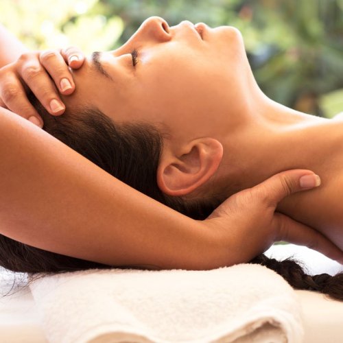 A person receiving a relaxing massage, with hands gently supporting their head and neck. Soft, serene background.
