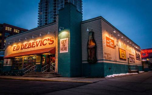 A brightly lit diner named Ed Debevic's, featuring retro signage and a Coca-Cola advertisement, at dusk.