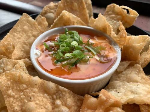A bowl of spicy dip topped with green onions, surrounded by crispy tortilla chips.