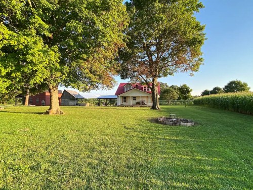 A scenic view of a grassy yard with trees, a house, and barns under a clear blue sky.